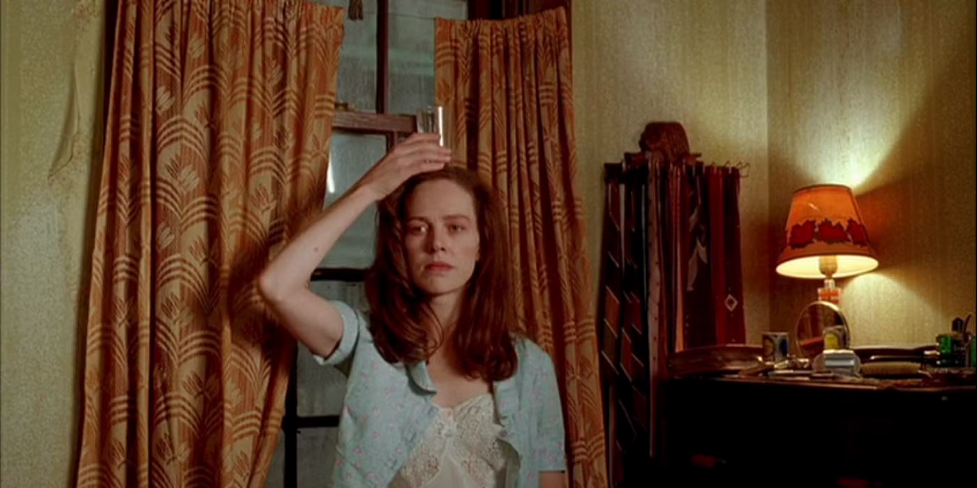 Inside an apartment a woman places a glass atop her head.