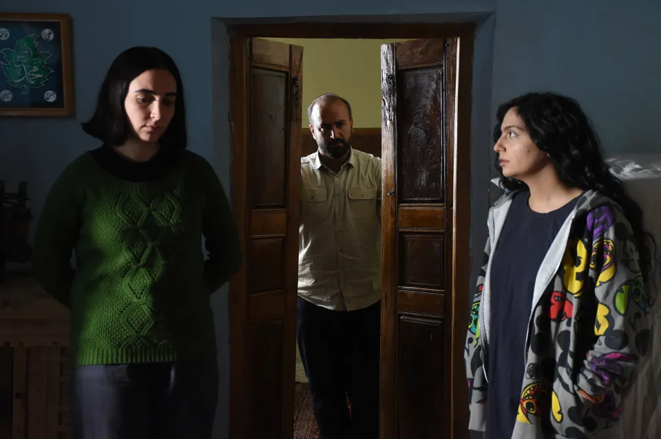 At either side, a teenage girl and her younger sister. Between them, standing in a double doorway, their father.